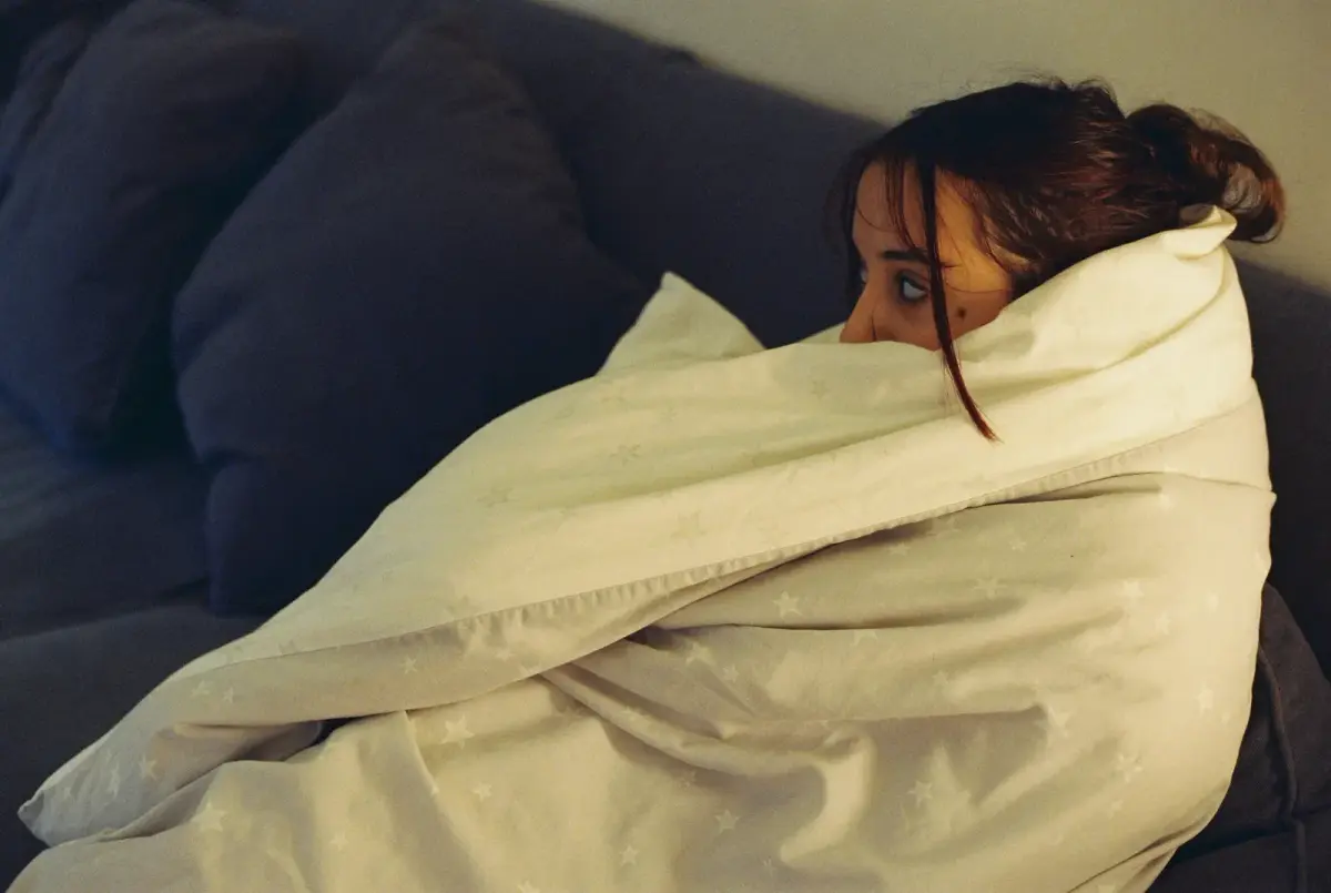 A woman wrapped in a blanket, resting on a sofa at home