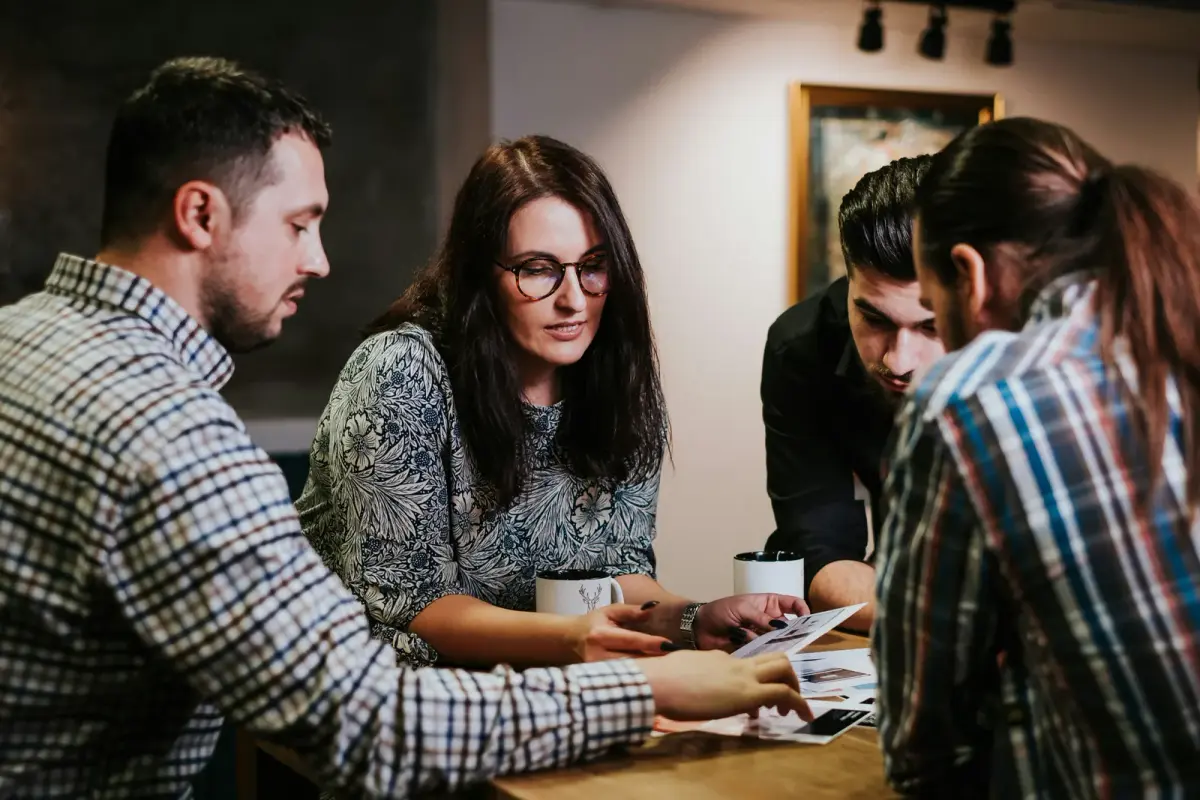 Four coworkers going through printed pages together at a wooden table