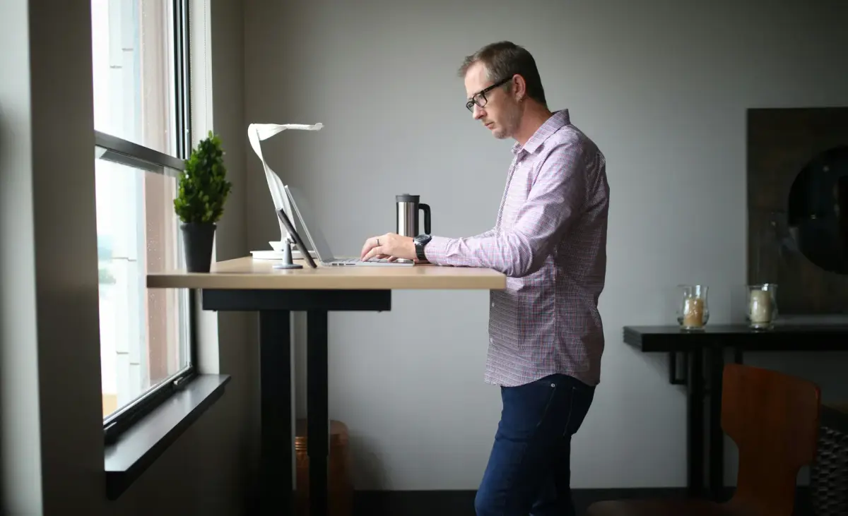 A man working on a laptop at a standing desk by a window