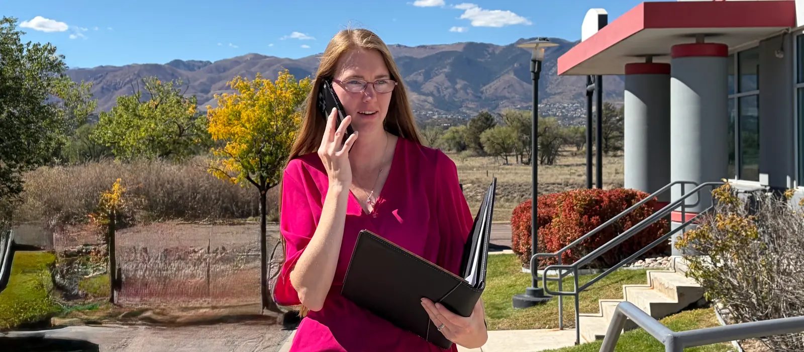 Allisha McCartney on the phone with a folder in her hand, mountains behind her